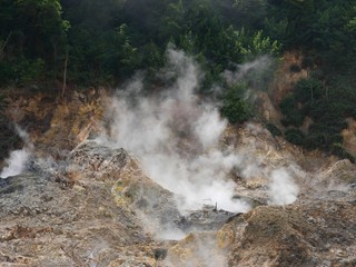 Fototapeta na wymiar Close up of smoke rising up from the craters at the drive-thru volcano at the Sulphur Springs in St Lucia, Caribbean Islands