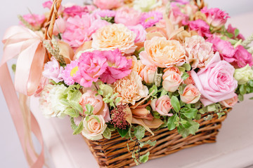 flowers arrangement with various of colors in wicker basket on pink table. beautiful spring bouquet. bright room, white wall. copy space