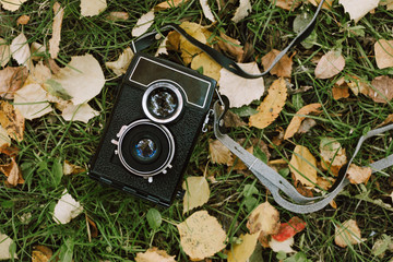 Flatlay of vintage two-lens camera on green grass and yellow leaves in forest