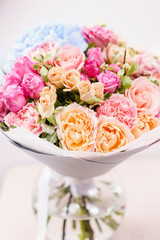 beautiful spring bouquet. flowers arrangement with various of colors in glass vase on pink table. bright room, white wall.