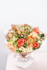 beautiful spring bouquet. flowers arrangement with various of colors in glass vase on pink table. bright room, white wall