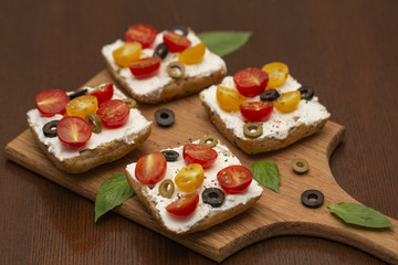 Sandwich with cottage cheese, tomatoes, olives and Basil on wooden background