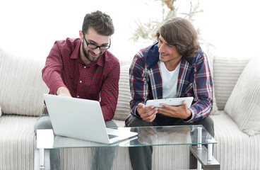 two young men working with laptop and tablet sitting on couch