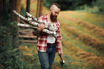 Bearded mohawk Man with firewoods and with axe on shoulder