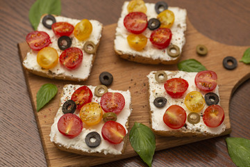 Sandwich with cottage cheese, tomatoes, olives and Basil on wooden background
