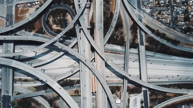 Top view drone rising above incredible complex highway junction in Los Angeles with traffic moving on multiple levels.