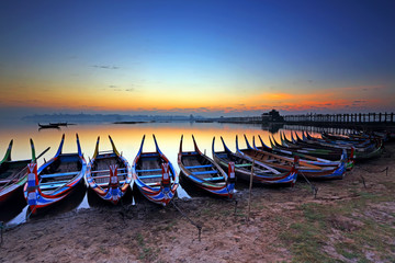 Colorful of old wooden boats in lake at during sunrise. World longest wooden bridge at U Bein bridge, Mandalay, Myanmar 