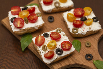 Sandwich with cottage cheese, tomatoes, olives and Basil on wooden background