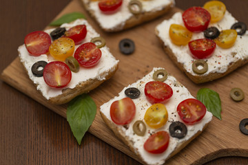Sandwich with cottage cheese, tomatoes, olives and Basil on wooden background