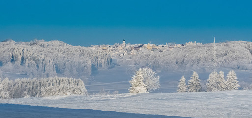 A small village in the deepest winter on the Swabian Alb in Germany with blue sky and snowy landscape.