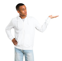 Dark-skinned young man with white sweatshirt holding copyspace imaginary on the palm to insert an...