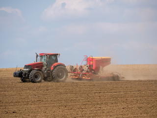Obraz premium Tractor with a modern sowing seeds machine in a newly plowed field. Plowed land as a background. Red tractor on the field.