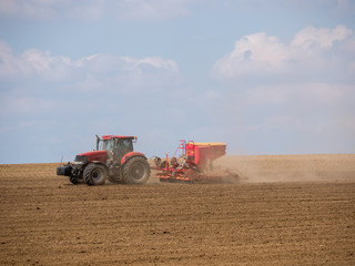 Tractor with a modern sowing seeds machine in a newly plowed field. Plowed land as a background. Red tractor on the field.