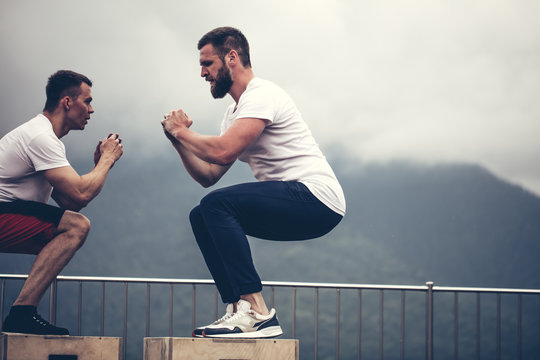 Cross-fit male athletes doing plyometric exercise. Jumping on the box. Phase touchdown, close up. Outdoor workout over mountains and foggy sky background