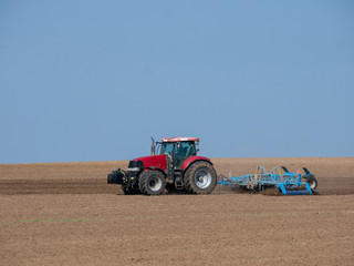 Obraz premium Red tractor with plow on the field. Tractor on the field. Summer field and red tractor.