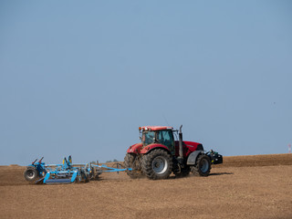 Red tractor with plow on the field. Tractor on the field. Summer field and red tractor.