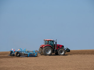 Obraz premium Red tractor with plow on the field. Tractor on the field. Summer field and red tractor.
