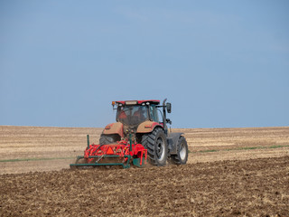 Obraz premium Red tractor with plow on the field. Tractor on the field. Summer field and red tractor.