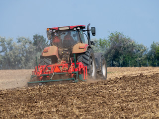 Fototapeta premium Red tractor with plow on the field. Tractor on the field. Summer field and red tractor.