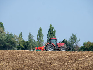 Obraz premium Red tractor with plow on the field. Tractor on the field. Summer field and red tractor.