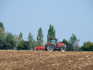 Red tractor with plow on the field. Tractor on the field. Summer field and red tractor.