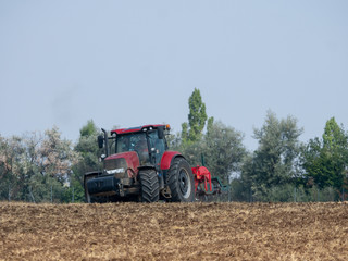 Obraz premium Red tractor with plow on the field. Tractor on the field. Summer field and red tractor.