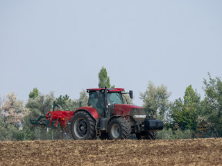Obraz premium Red tractor with plow on the field. Tractor on the field. Summer field and red tractor.