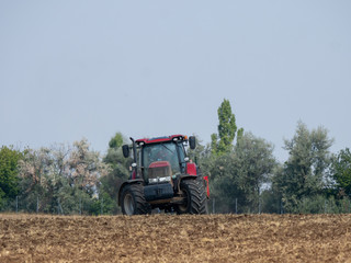 Obraz premium Red tractor with plow on the field. Tractor on the field. Summer field and red tractor.