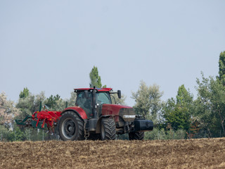 Red tractor with plow on the field. Tractor on the field. Summer field and red tractor.