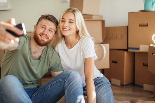 young couple moving together in new house , unpacking cardboard boxes, taking selfie