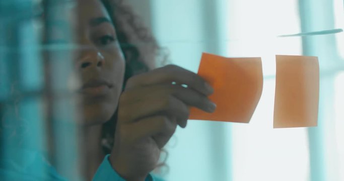 African American black employee looking onto a glass wall with sticky notes, framework for managing work, scrum methodology. 4K UHD 60 FPS SLOW MOTION