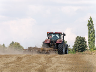 Fototapeta premium Red tractor with plow on harvest field. Summer field and red tractor. Tractor on harvest field. Lowing after harvest. Plowing on the field.