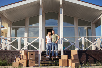 Husband and wife standing in front of new buying home with boxes. bought first home