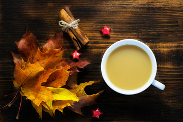 Mug of hot coffee with milk and spices and autumn leaves on wooden table. Morning cup of cappuccino coffee with cinnamon and maple leaves.