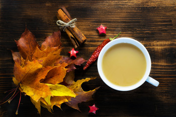 Mug of hot coffee with milk and spices and autumn leaves on wooden table. Morning cup of cappuccino coffee with cinnamon and maple leaves.