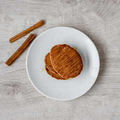 Still life morning breakfast of pancakes with honey and cinnamon sticks on a white plate on a wooden background