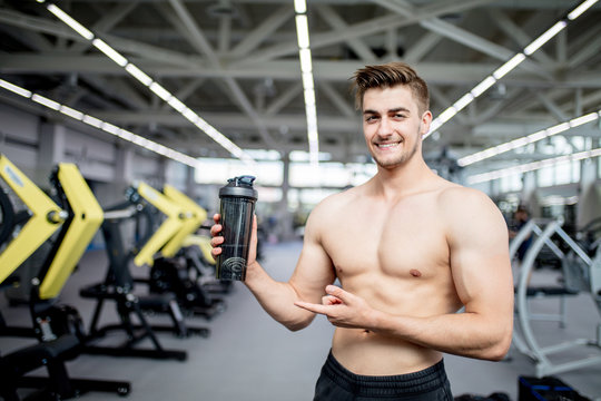 Athlete man having a snack with protein cocktail in shaker over gym machine background