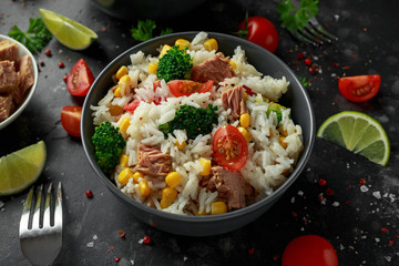 Fresh Tuna rice salad with sweet corn, cherry tomatoes, broccoli, parsley and lime in black bowl