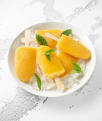 Popsicles, ice lollies on stick with sweet orange juice in white plate with ice