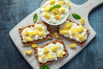 Homemade Crispbread toast with Cottage Cheese and Pineapple on white wooden board.