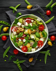 Healthy low calories salad with lettuce, heirloom tomatoes, avocado, feta cheese, red onion, cucumber, sweet peas, olives, thyme, mint and basil.