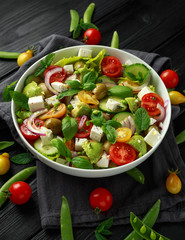 Healthy low calories salad with lettuce, heirloom tomatoes, avocado, feta cheese, red onion, cucumber, sweet peas, olives, thyme, mint and basil.