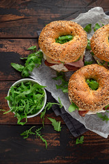 Fresh Bagels Sandwiches with cream cheese, bacon, tomato and green wild rocket on rustic wooden table
