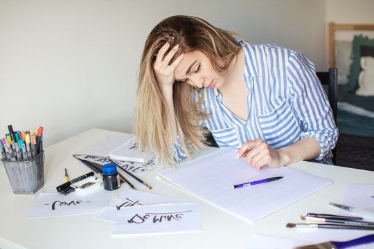 Tired sad calligraphy female artist sitting at desk