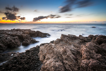 A long exposure shot of a sea at dusk with boulders as foreground and a combination of warm and blue colors in the sky. Taken at Wakamatsu Fishing Park, Kitakyushu, Fukuoka, Japan