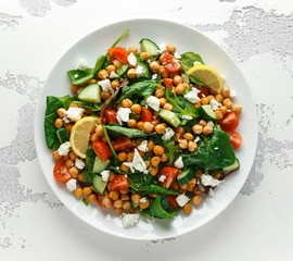 Chickpeas Salad with cucumber, tomatoes, feta cheese and green mix in a white plate. healthy food.