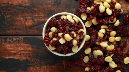 Healthy snack of Dried cranberries and macadamia nuts in a ceramic bowl on rustic wooden table