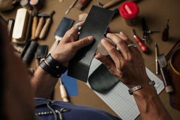 Details of work at leather workshop nowdays. High angle of man s hands closeup, dealing with modern...