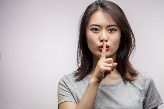 Asian female model keeping index finger near mouth making hush sign. Closeup portrait of young Korean woman demands silence, respecting woman s secret