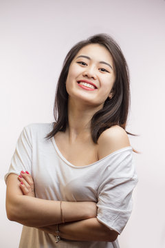 Asian smiling joyfully female with dark loose hair, dressed casually, looking with satisfaction at camera, being happy. Studio shot of appealing Korean woman isolated against blank wall.